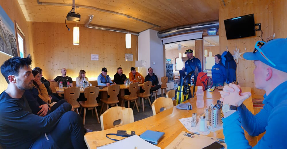 Téli magashegyi tanfolyam - 3 nap az Alpokban MountainGo módra 15 Téli magashegyi tanfolyam résztvevői körben ülnek és a vezető oktatót előadását figyelik